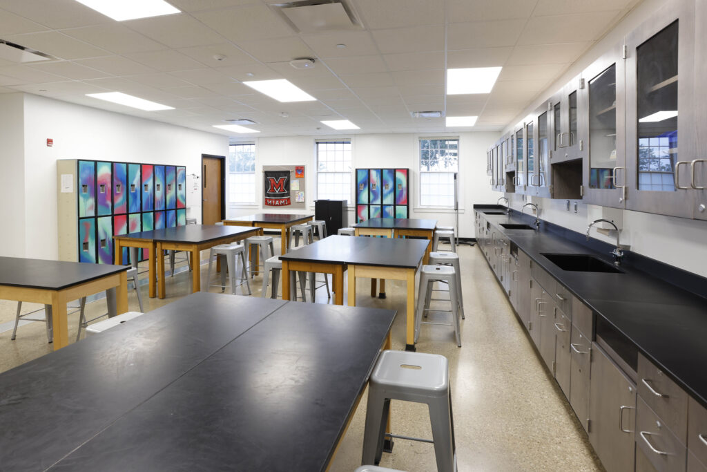 A science laboratory with black-topped work tables, metal stools, cabinets, and lockers with colorful patterns.