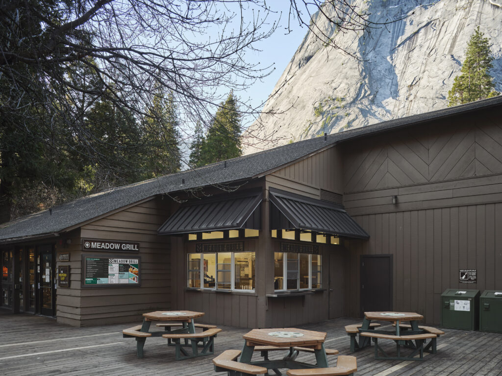 The Meadow Grill building with outdoor picnic tables, set against a large mountain cliff.