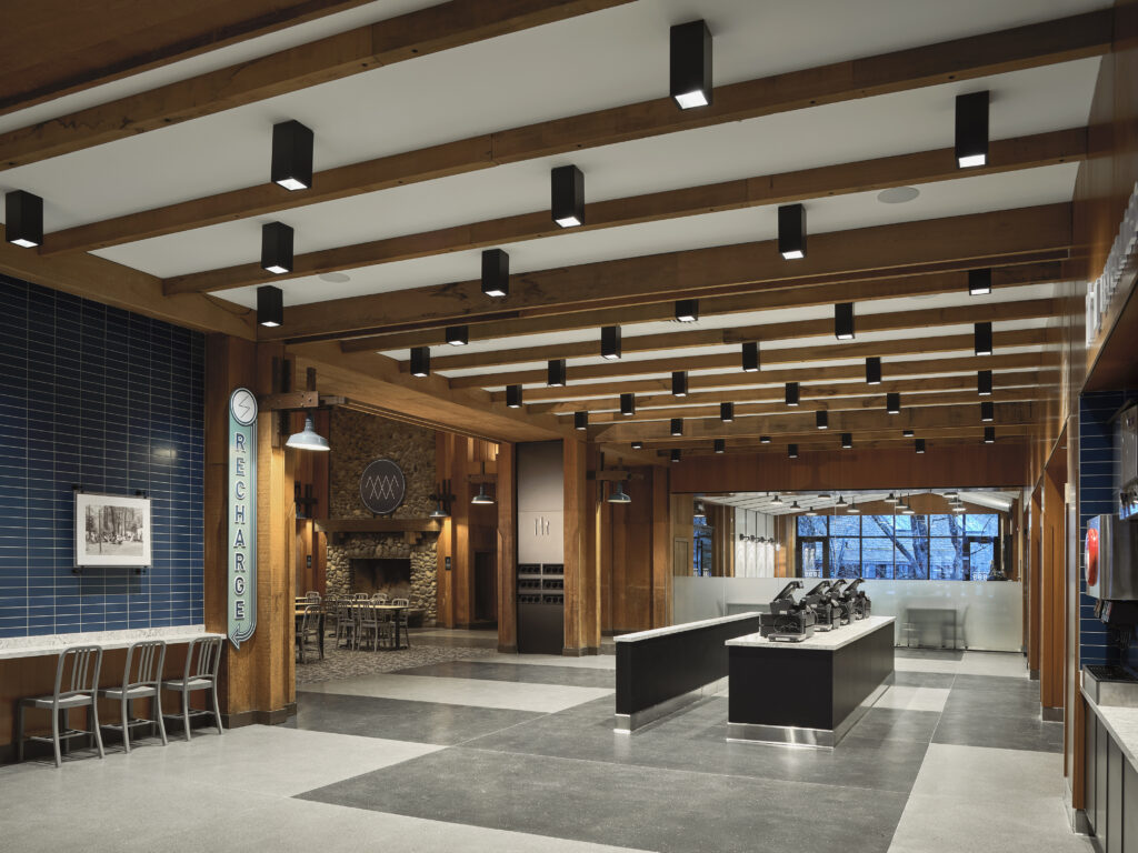 Interior of a modern lounge featuring a “RECHARGE” sign, bar seating, a stone fireplace, and a service counter.