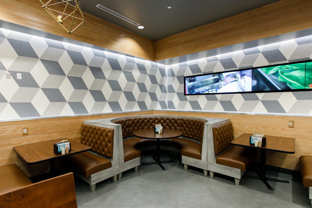 Corner booths with brown tufted seating and wooden tables in a restaurant with geometric wall patterns.