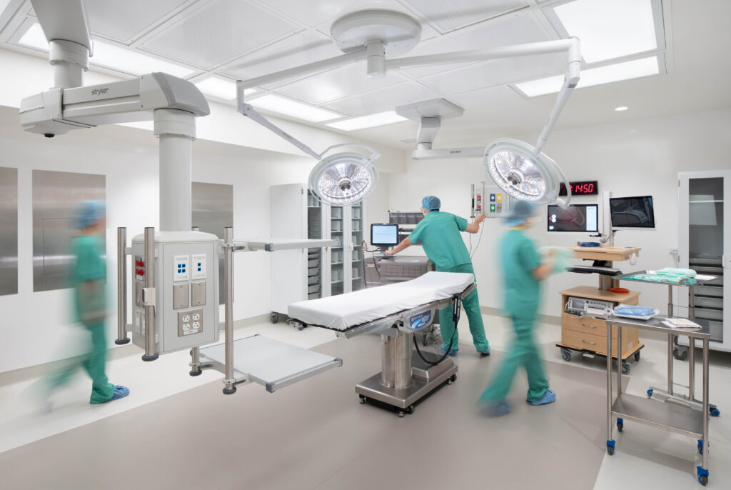 Medical staff in scrubs working in a modern operating room with an examination table and overhead surgical lights.