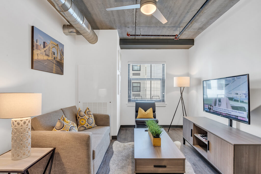 A living room with a gray sofa, a wood coffee table with a small plant, an armchair, and a wall-mounted television.