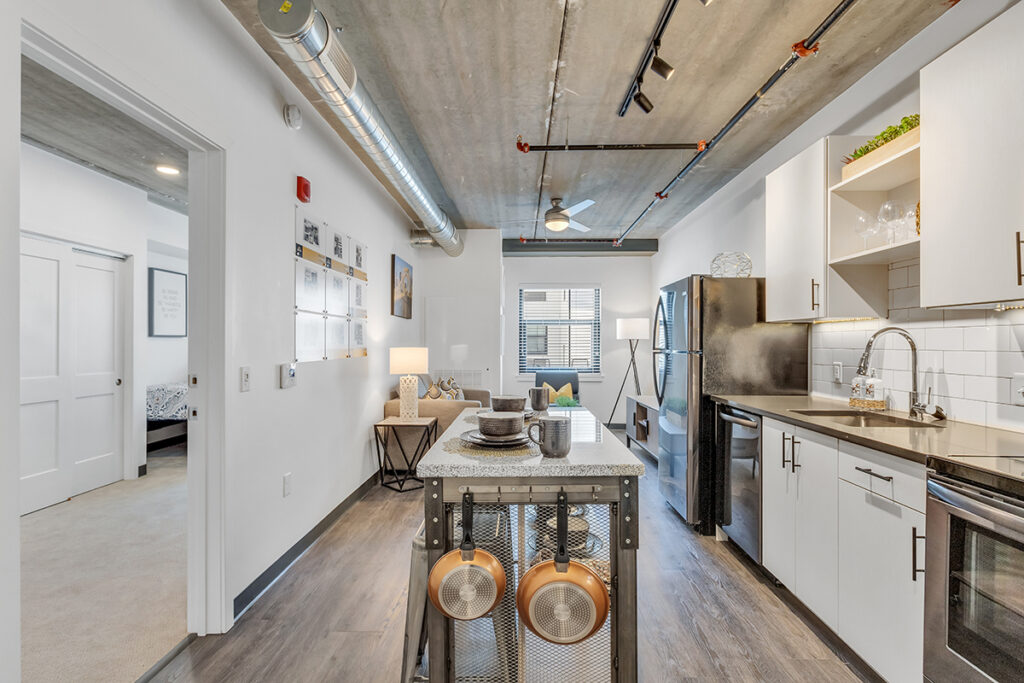 A kitchen featuring a central island with hanging copper pots, white cabinets, and stainless steel appliances under an exposed concrete ceiling.