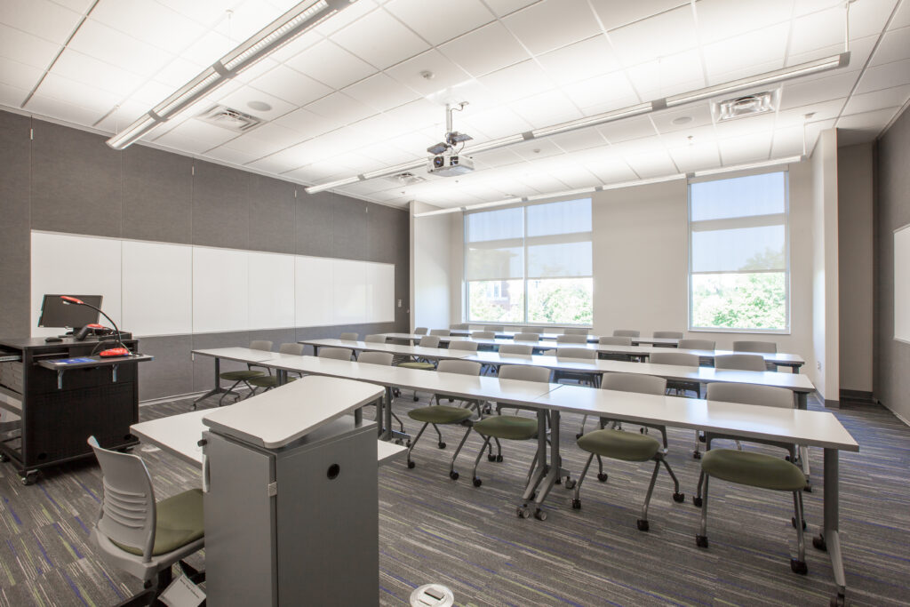 A classroom with rows of desks and chairs facing a whiteboard and a teaching podium.