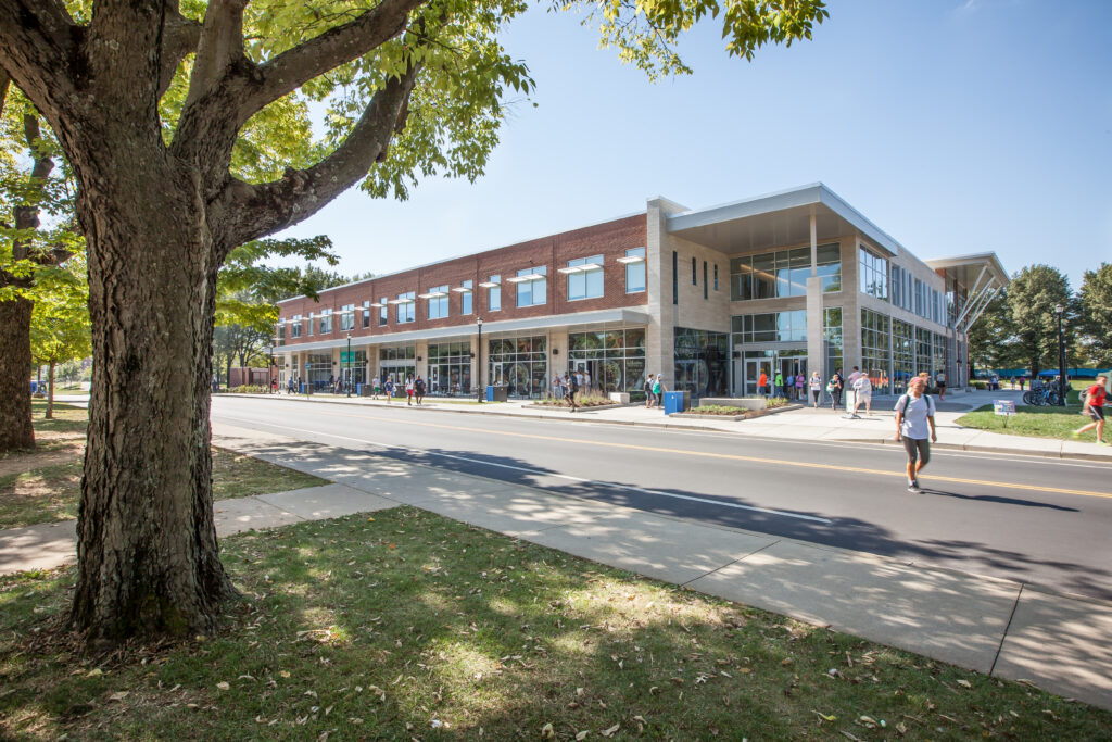 Modern brick and glass university building with students walking along the sidewalk.
