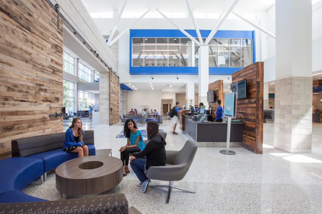 Students gather in a bright, modern university student union building with lounge seating and a service desk.