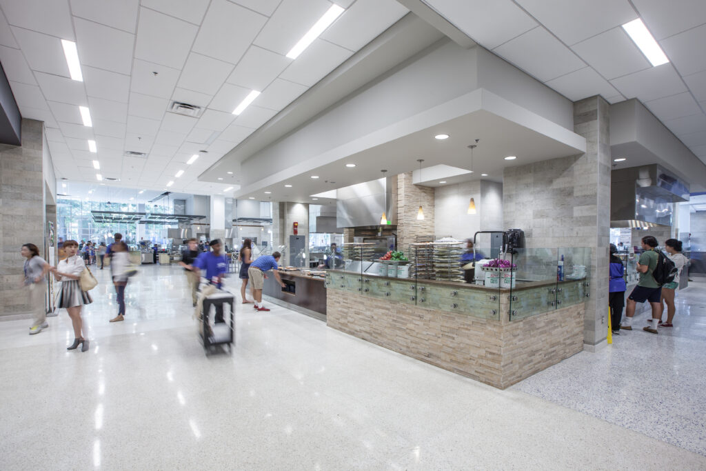 People walking through a modern university dining hall with a food service counter.