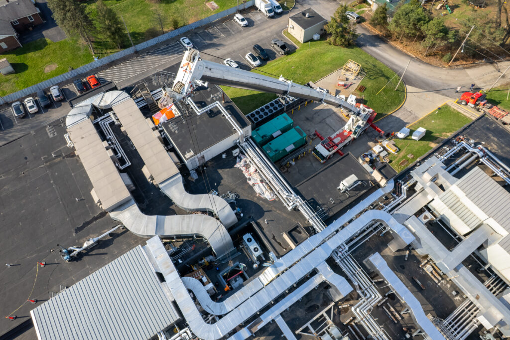 Aerial view of a crane lifting equipment onto a flat commercial roof covered in HVAC ductwork.