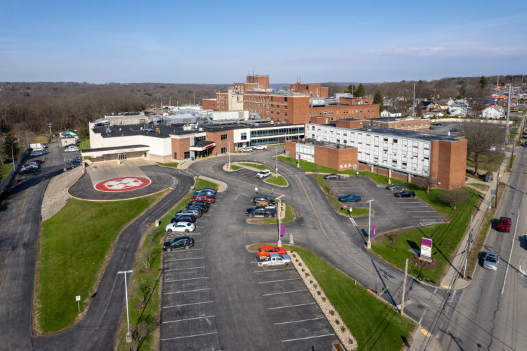 Aerial view of a hospital complex with multiple brick buildings, parking lots, and a helipad.