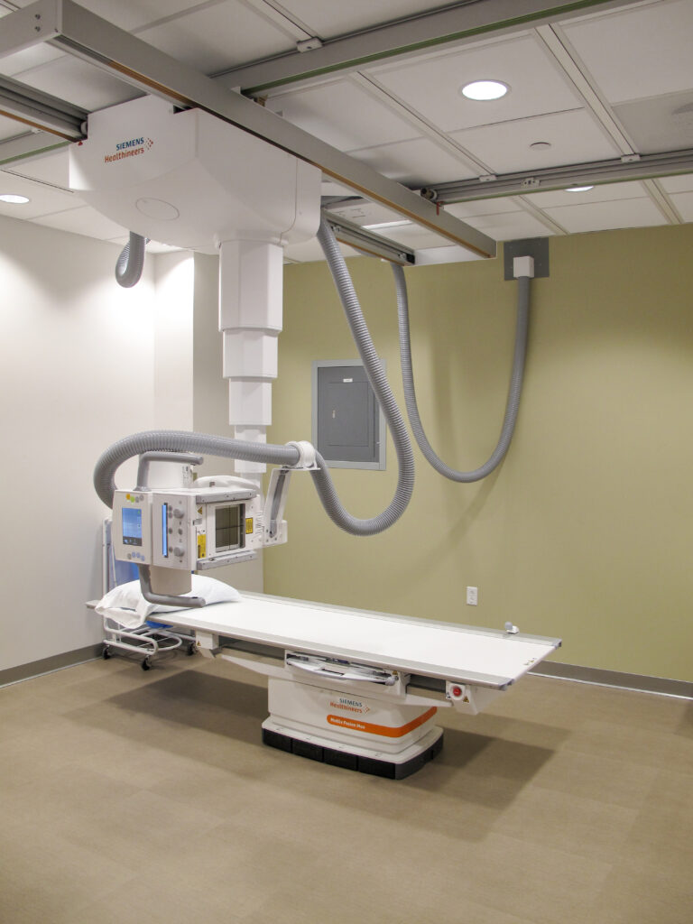 Siemens Healthineers radiography imaging system with an adjustable examination table and ceiling-mounted X-ray tube.