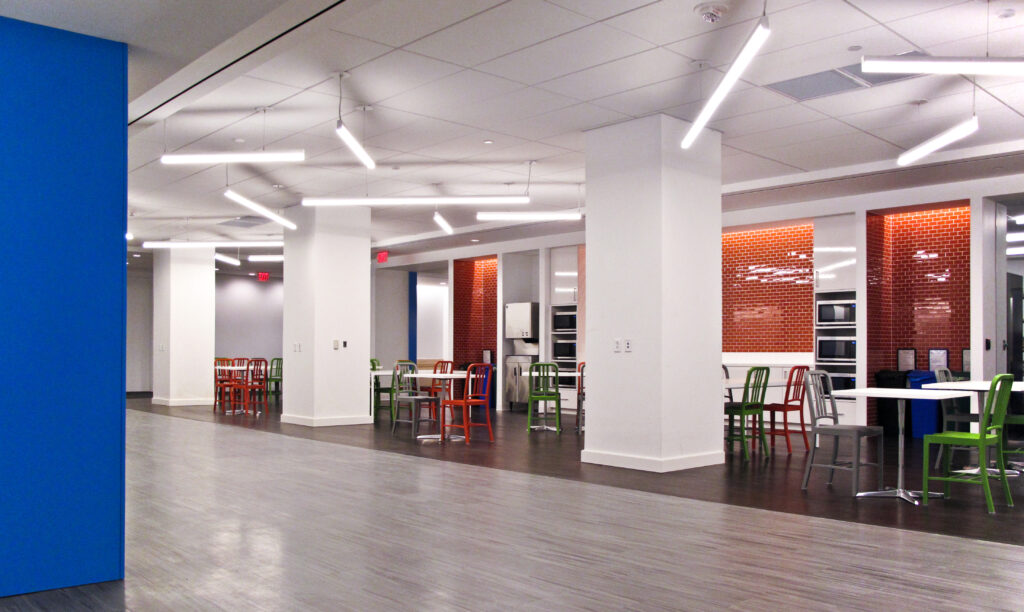 A large, modern breakroom with multiple tables and colorful chairs arranged in clusters.