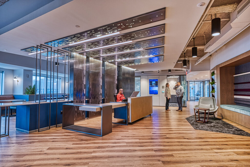 A modern office lobby with a receptionist desk, a man and woman conversing, and a small seating area.