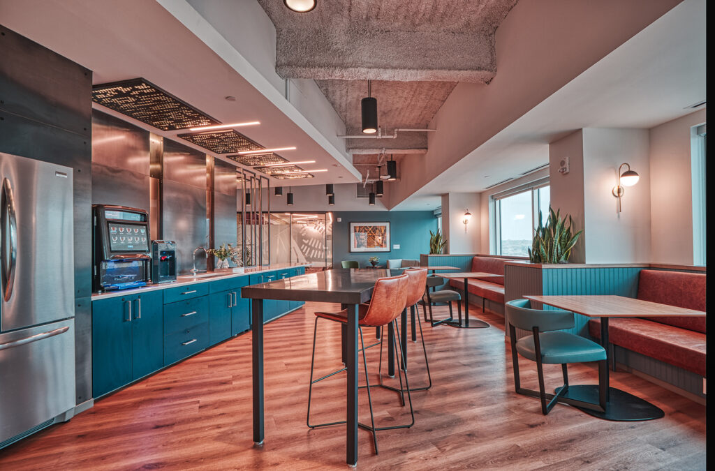 Modern office breakroom with a kitchen counter, beverage station, high-top table with stools, and booth seating.