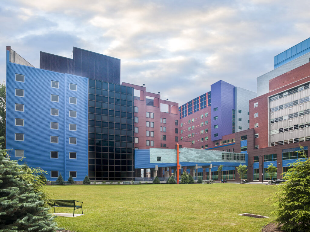 Large complex of multi-colored buildings in blue, red, and purple with a central grass courtyard.