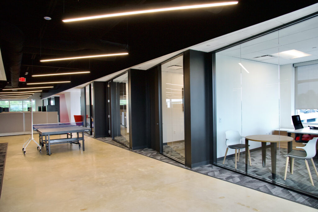Open office space featuring a blue ping-pong table and a glass-walled meeting room with a round table and two chairs.