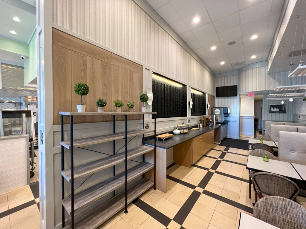 A multi-level metal and wood shelving unit in a restaurant, next to a service counter with a beverage machine and dining area.