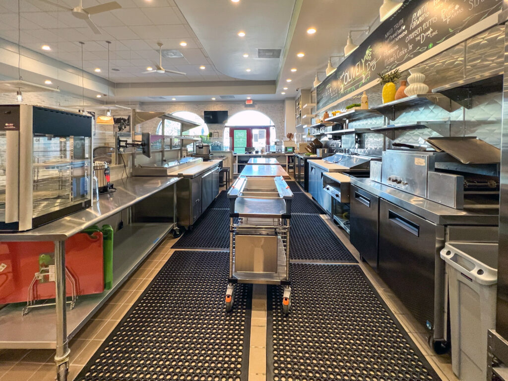Commercial kitchen interior with stainless steel counters, industrial equipment, and a chalkboard menu on the wall.