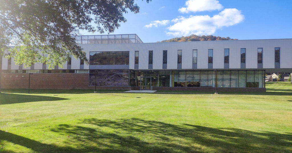 A two-story modern building with vertical panels and glass windows, situated behind a wide green lawn.