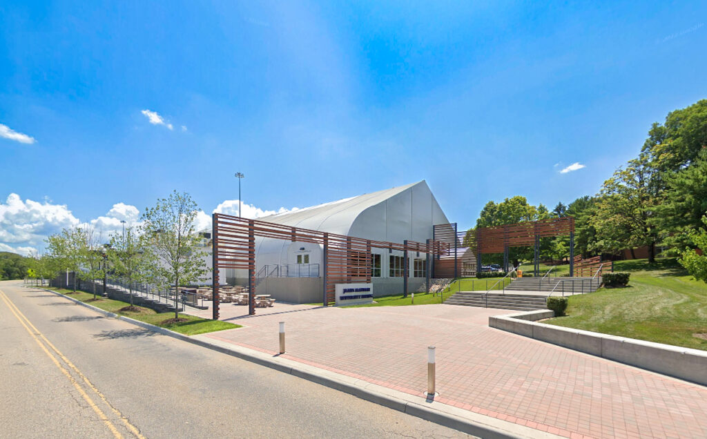 James Madison University softball facility building with a white arched roof, outdoor seating, and wood slat accents.