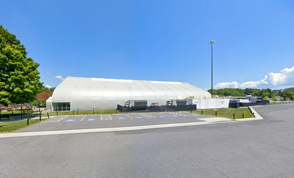 A large, white, arched fabric structure with an adjacent parking lot featuring several accessible parking spaces.