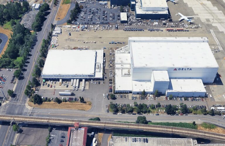 Aerial view of a Delta aircraft maintenance facility with two large hangars next to an airport tarmac.