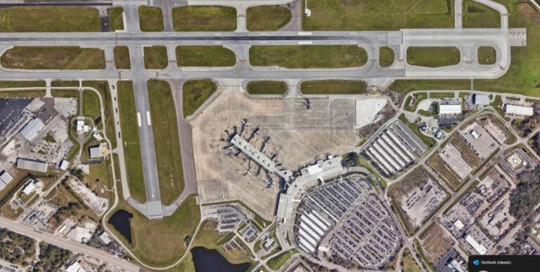 Aerial view of an airport terminal with parked airplanes, surrounding runways, and parking lots.