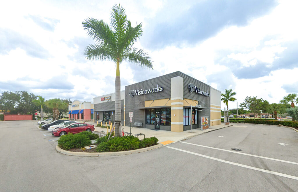 Exterior view of a Visionworks store in a shopping plaza with a parking lot and palm trees.
