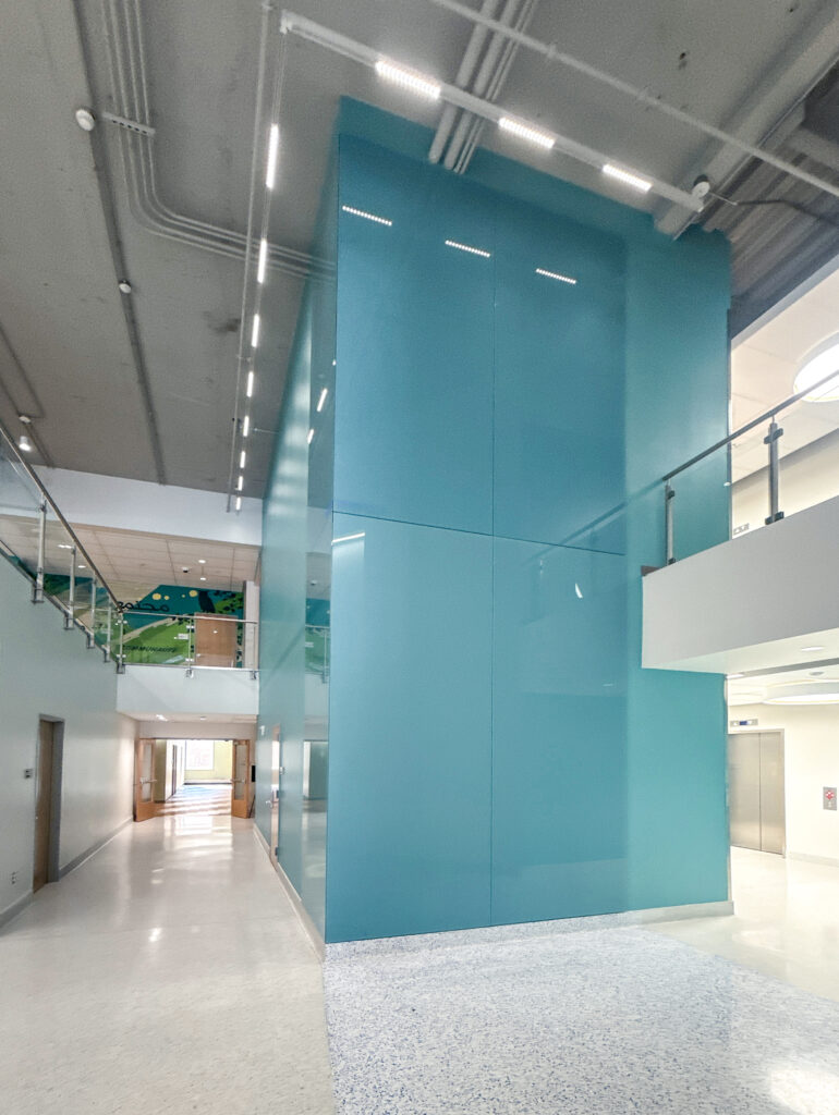 A tall, glossy turquoise feature wall in a multi-level building hallway.