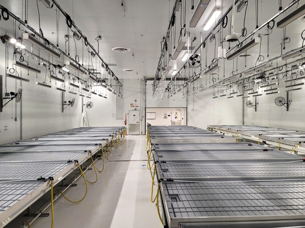 A clean, industrial indoor facility with rows of metal grow tables and overhead hanging lights.