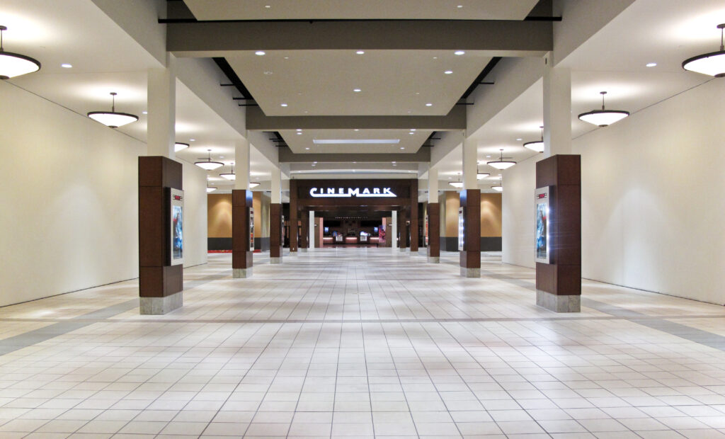An empty hallway in a shopping mall leading to a Cinemark movie theater entrance.