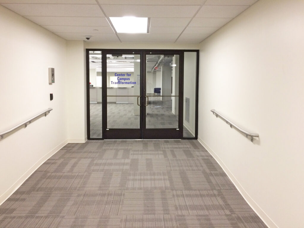 Double glass doors leading to an office suite labeled “Center for Campus Transformation,” viewed from a hallway with handrails on both walls.