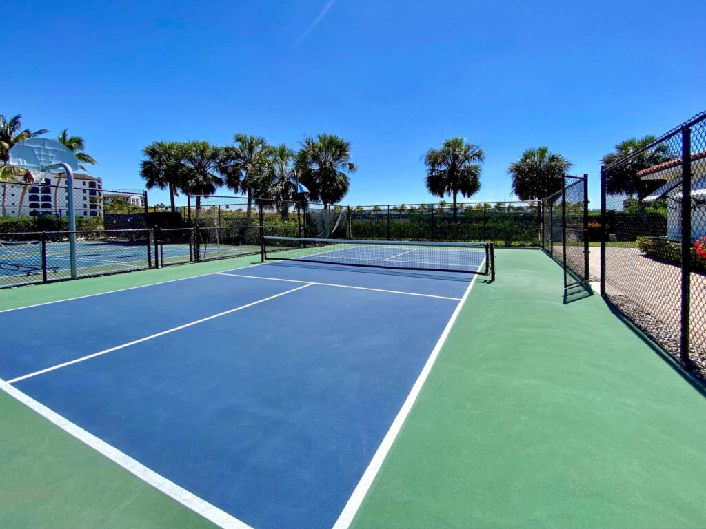 An outdoor blue and green pickleball court enclosed by a chain-link fence under a clear blue sky.