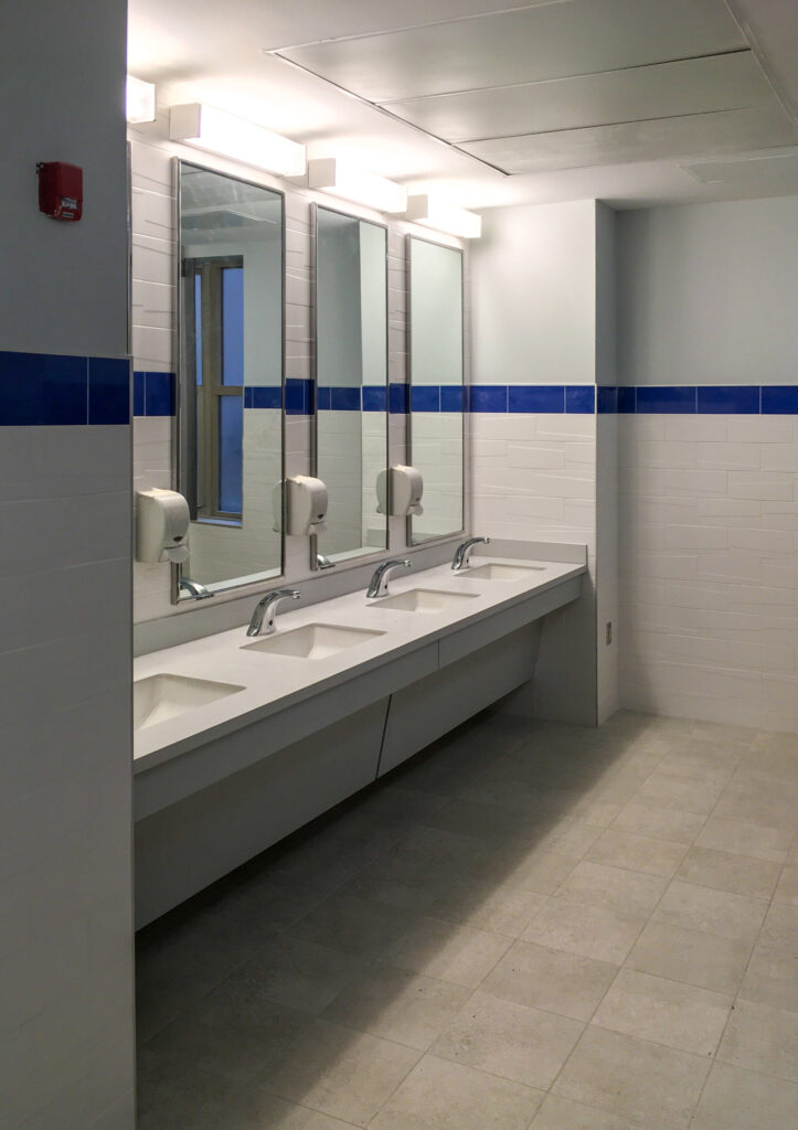 A public restroom vanity with three sinks, chrome faucets, and soap dispensers mounted on a wall with white and blue tiles.