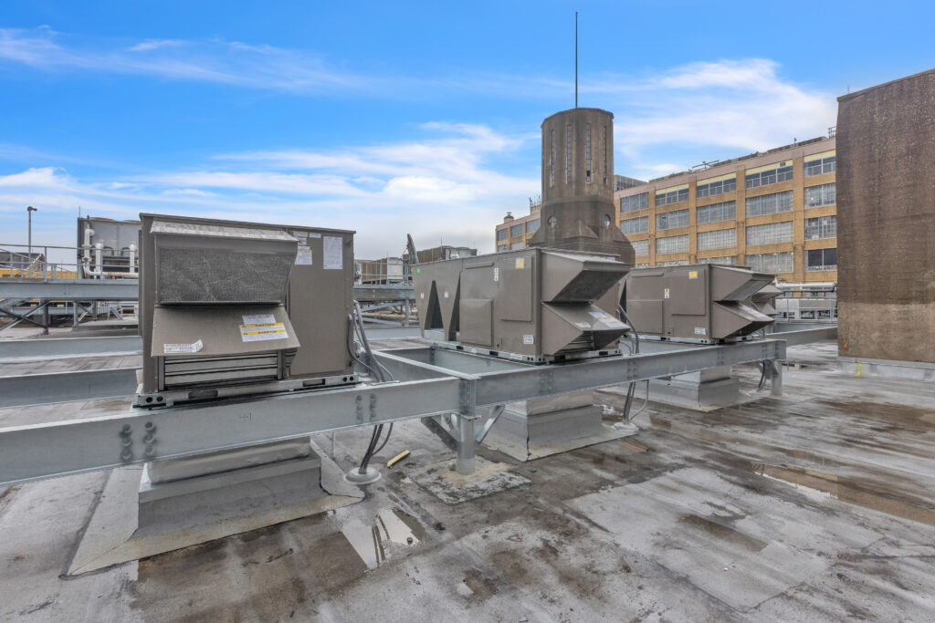 Three HVAC units mounted on a metal frame on a flat industrial rooftop.