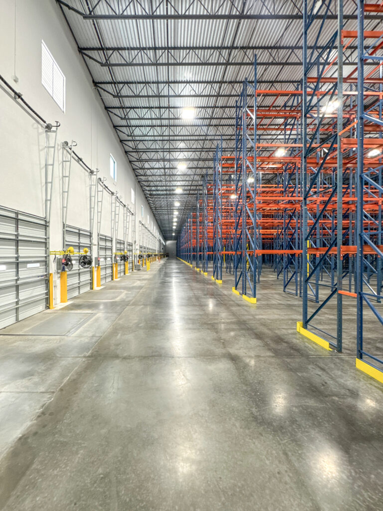A long, empty warehouse aisle lined with tall, blue and orange metal storage racks.