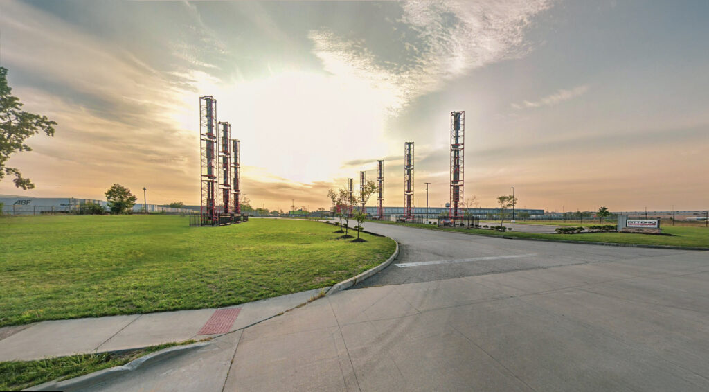A parking lot entrance at the Pitt Ohio facility, featuring a row of tall metal towers under a sunset sky.