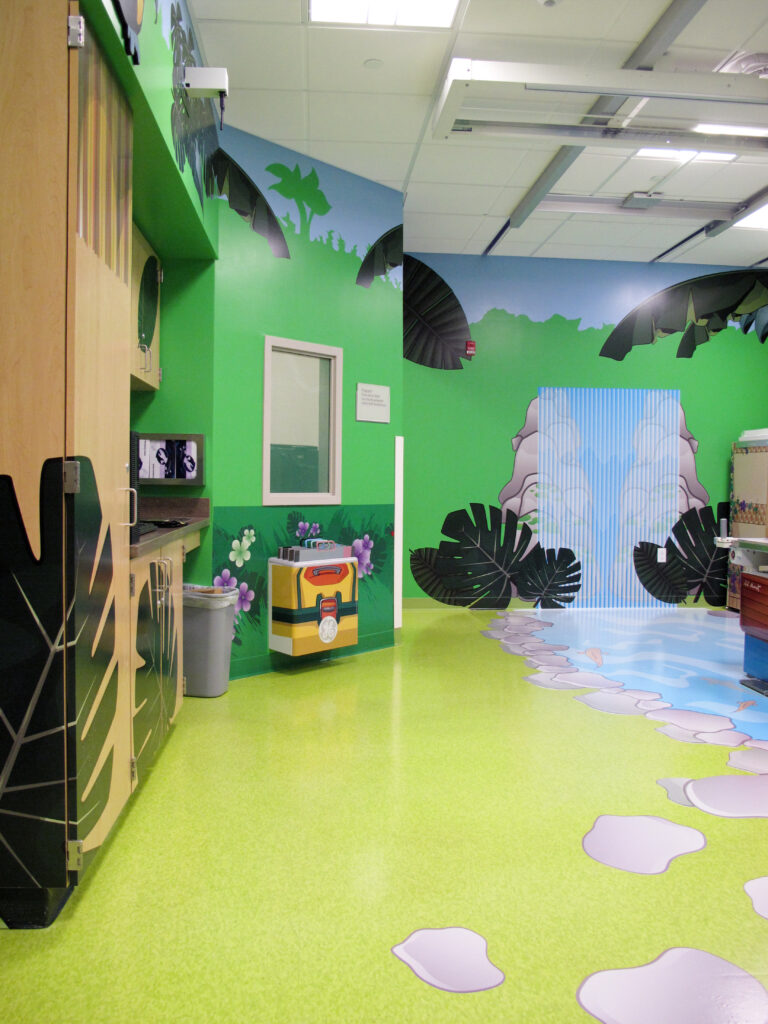 A colorful room decorated with a jungle theme, featuring a wall mural of a waterfall, tropical plants, and a bright green floor.