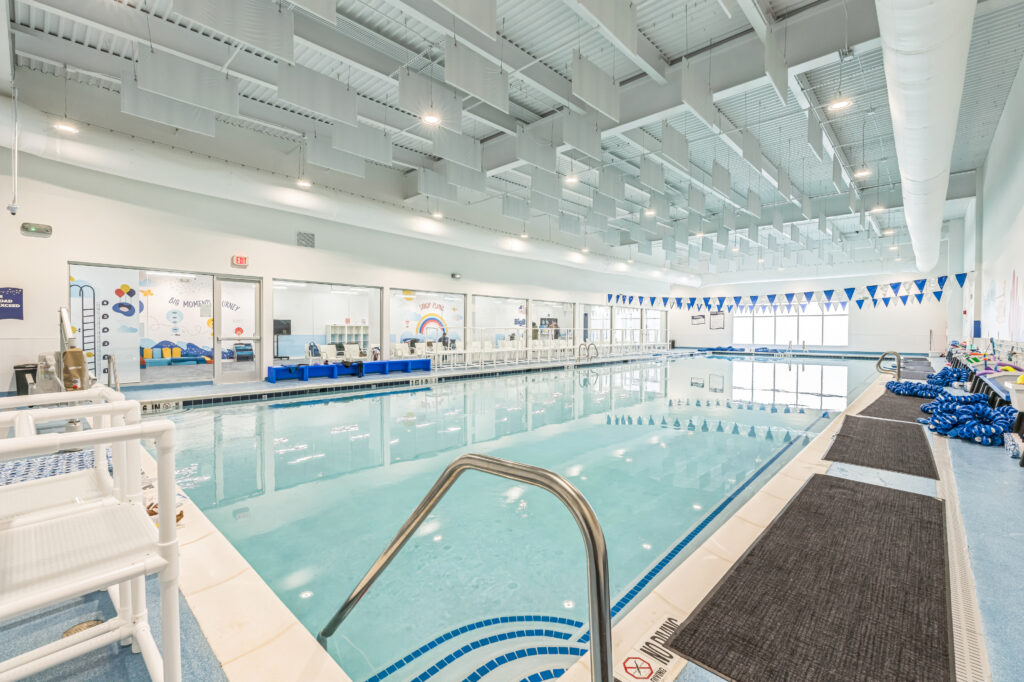 An indoor swimming pool with blue lane markers, a stainless steel handrail, and white acoustic panels hanging from the ceiling.