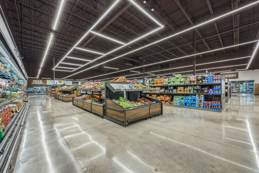 Interior view of a grocery store aisle featuring produce displays and shelves stocked with packaged food items.