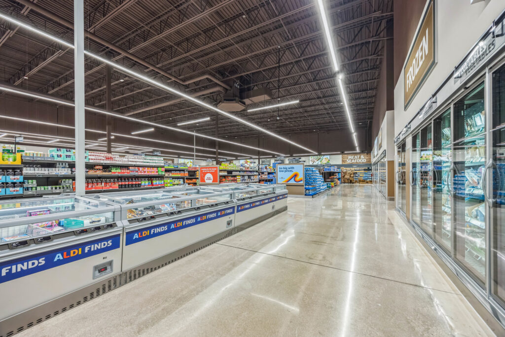 Interior of an Aldi grocery store featuring aisles of frozen food cases and refrigerated glass door displays.