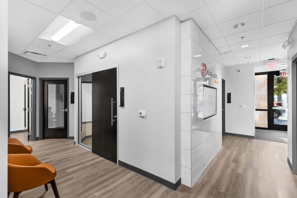 A modern office reception area with a tiled feature wall, glass-paned doors, and two orange chairs.