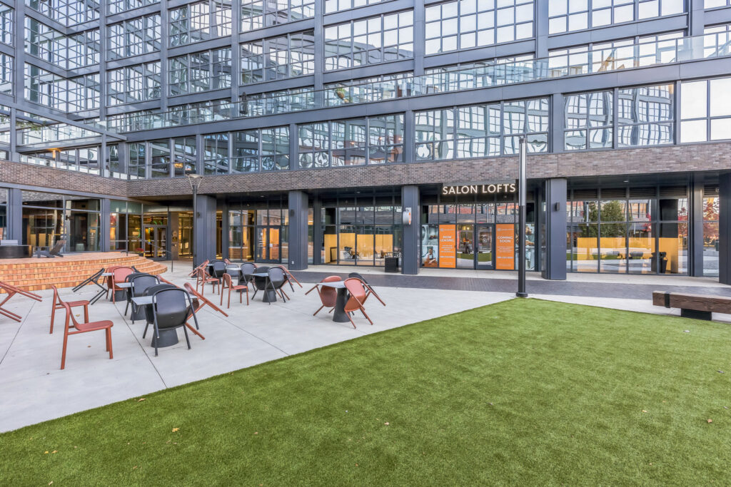 Outdoor patio with tables and chairs in front of a modern multi-story building featuring a Salon Lofts storefront.