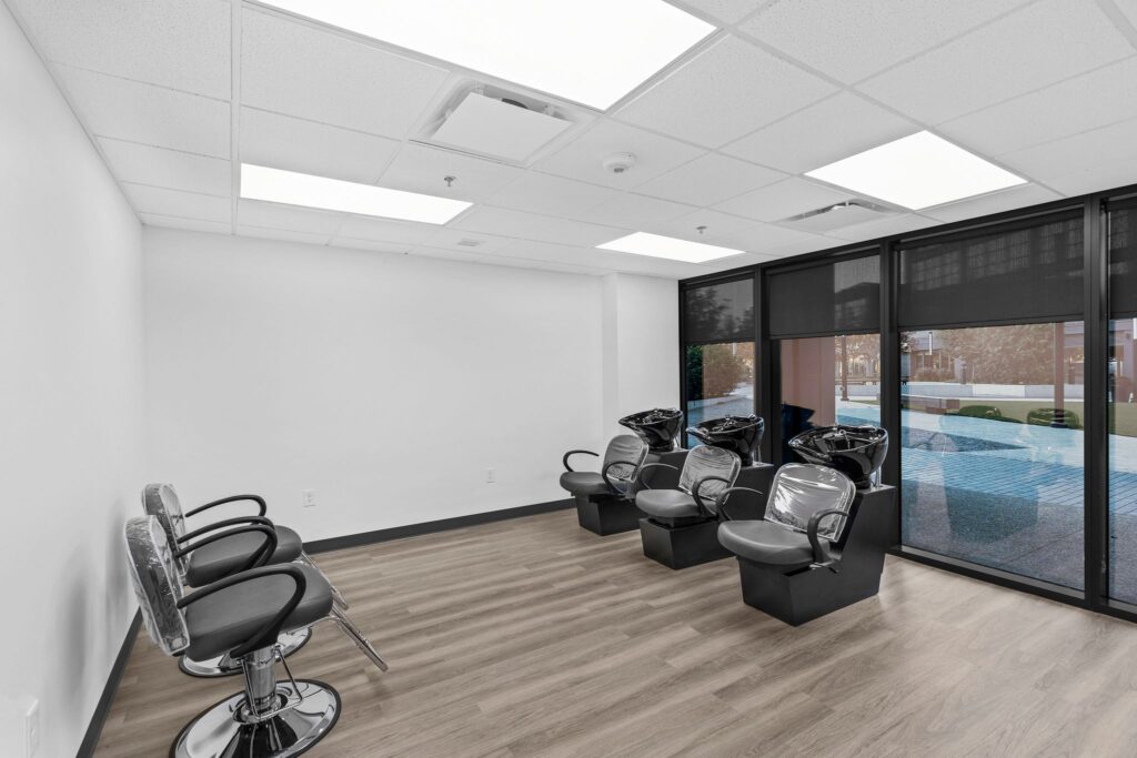 Hair salon interior with two styling chairs facing a blank wall and three black shampoo stations by a window.
