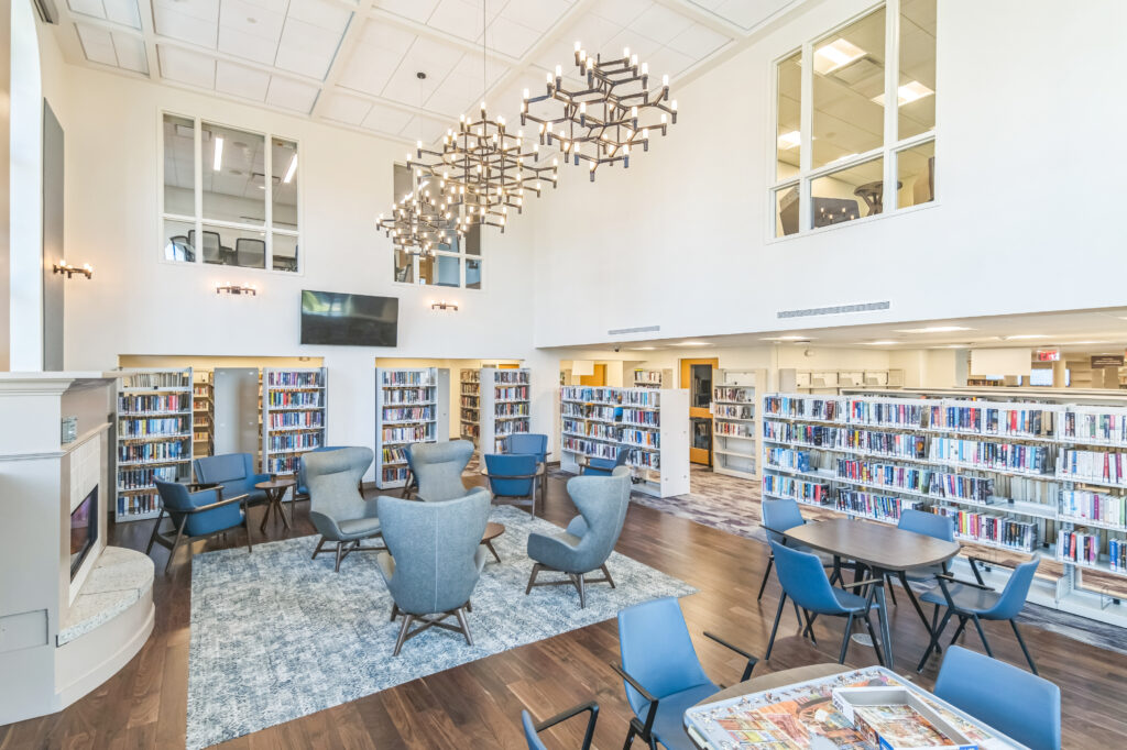 Modern library lounge with armchairs, bookshelves, and multi-tiered chandeliers.