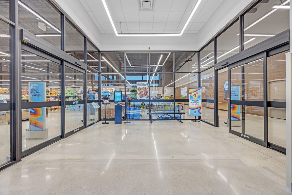 The entrance to an Aldi grocery store with glass sliding doors, a metal bench, and promotional signs.