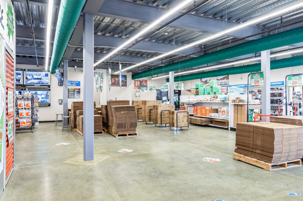 Interior of a retail store selling moving supplies, featuring stacks of flat-packed cardboard boxes on pallets and shelves of packing materials.