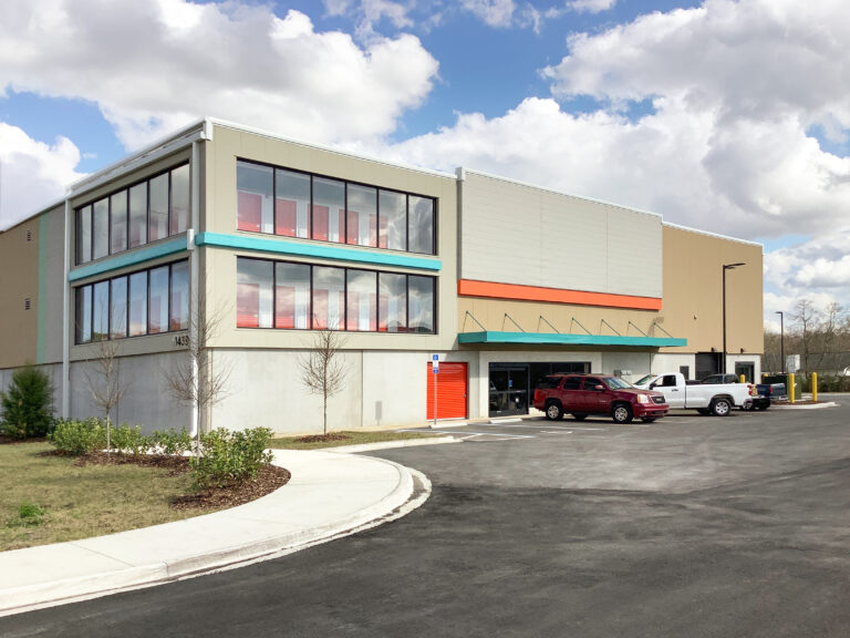 A multi-story self-storage facility with glass windows showing storage units and a parking lot with three vehicles.