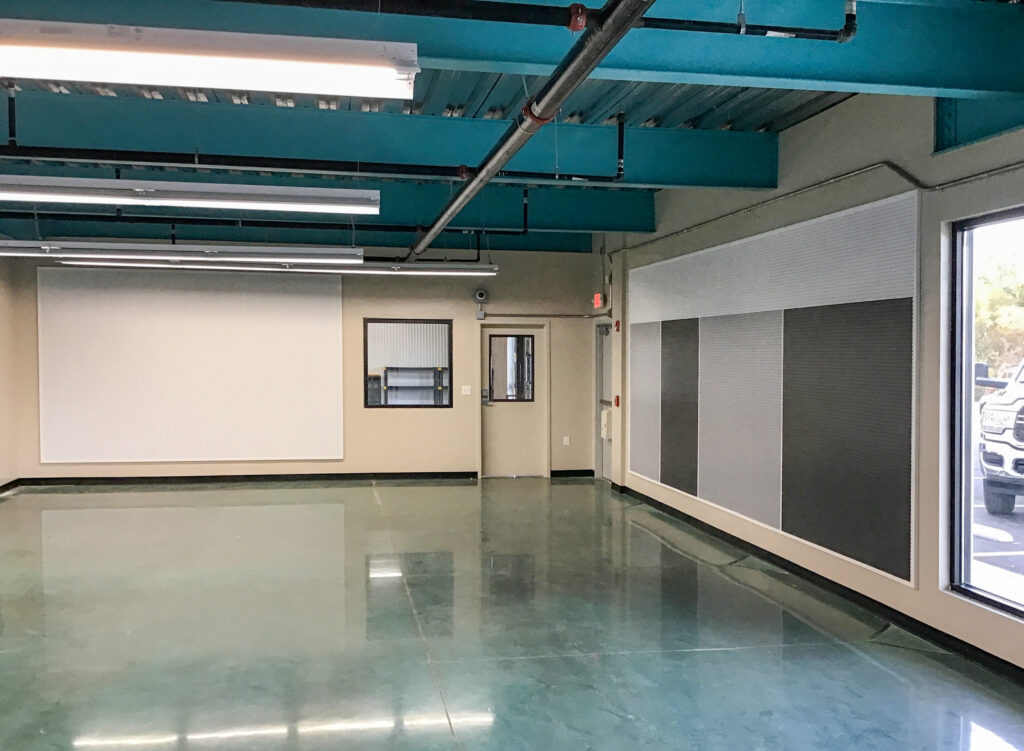 An empty room with a teal ceiling, reflective floor, and white and grey pegboard wall panels.