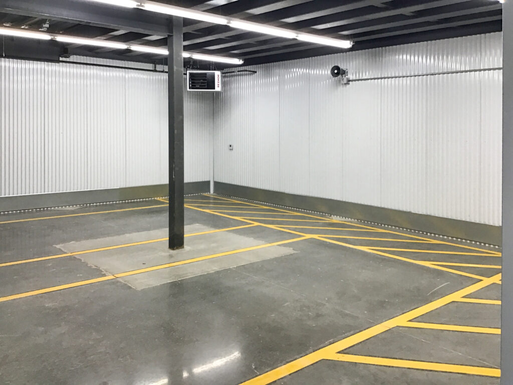 An empty garage or storage unit with a concrete floor, yellow painted floor markings, and a single support pillar in the center.
