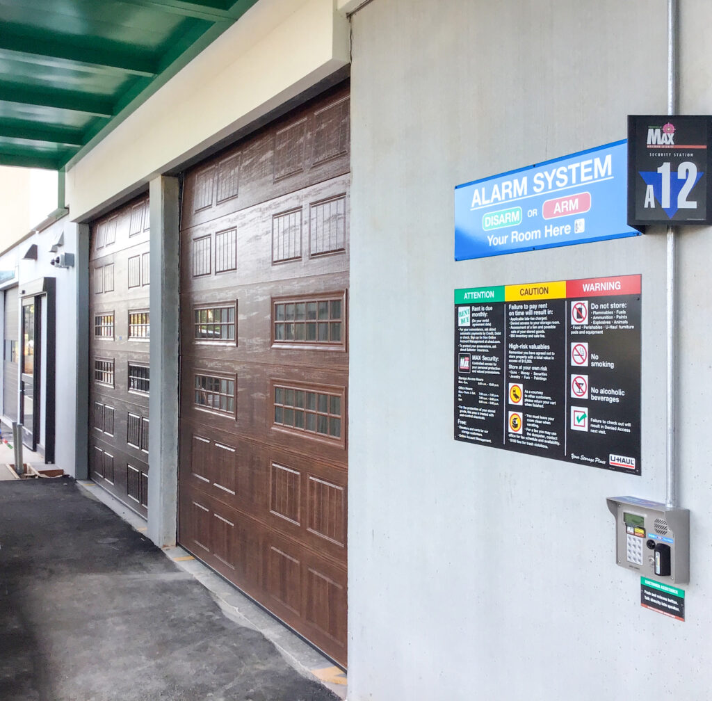 Storage unit facility entrance with two brown garage doors and a sign listing facility rules, alarm instructions, and a keypad.